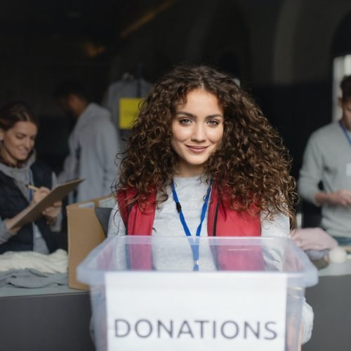 Woman volunteer working in community charity donation center, looking at camera